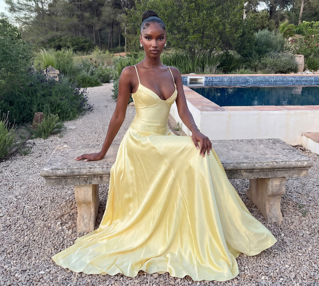 Butter yellow satin maxi dress, seated on a stone bench